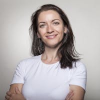 Portrait of a confident woman smiling with arms crossed, wearing a white t-shirt on a gray background.